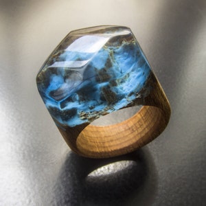 May include: A blue and brown resin ring with a wooden band. The resin has a swirling pattern and is set in a wooden band.