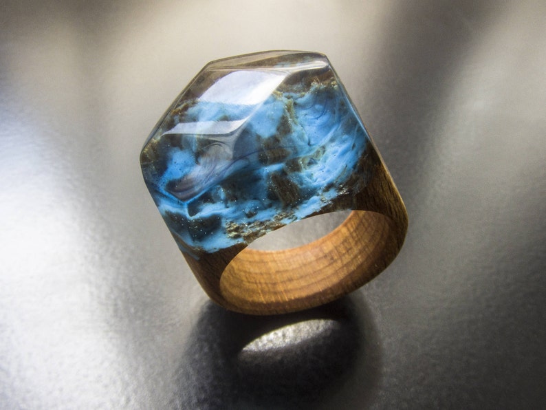 May include: A blue and brown resin ring with a wooden band. The resin has a swirling pattern and is set in a wooden band.