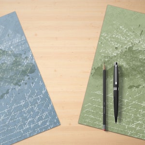 Puede incluir: Dos hojas de papel con texto escrito a mano sobre una superficie de madera clara. Una hoja es azul con texto blanco y la otra es verde con texto blanco. Un bol&iacute;grafo negro y un l&aacute;piz negro est&aacute;n sobre la hoja de papel verde.