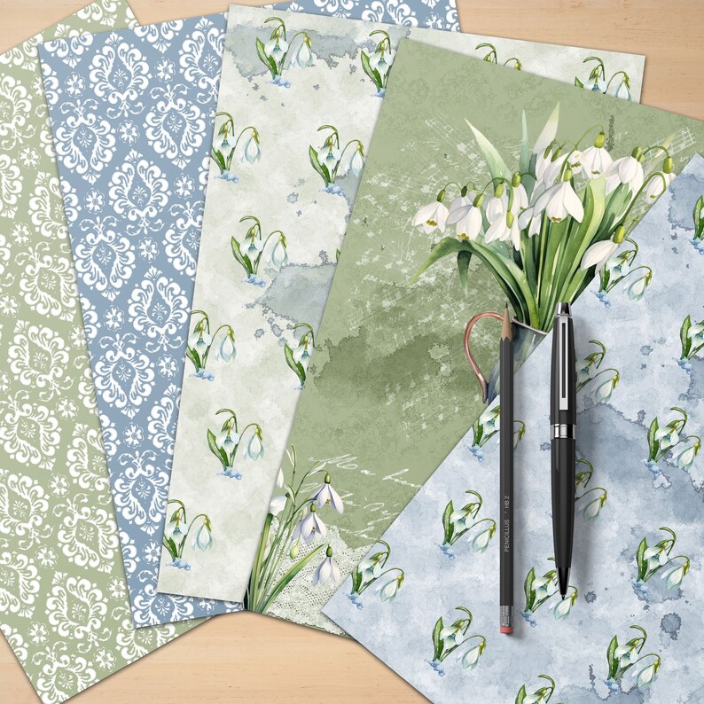 Puede incluir: Cinco hojas de papel decorativo con una variedad de patrones. Una hoja presenta un patr&oacute;n floral blanco sobre un fondo azul claro. Otra hoja presenta un patr&oacute;n floral blanco sobre un fondo verde claro. Las tres hojas restantes presentan un patr&oacute;n floral blanco sobre un fondo verde claro con acentos de acuarela.
