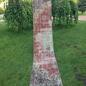 Pode incluir: Um tapete corredor vintage com um padrão floral desbotado em tons de vermelho, azul e creme. O tapete está colocado num relvado.