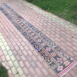 Puede incluir: Una alfombra larga y estrecha con un diseño persa tradicional. La alfombra tiene un fondo oscuro con intrincados patrones en tonos de rosa, naranja y azul. La alfombra está colocada en un camino de adoquines.