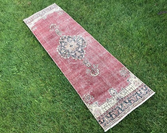 Puede incluir: Una alfombra roja vintage con un patrón floral blanco y negro. La alfombra tiene un borde con flecos y está colocada sobre una superficie de hierba verde.