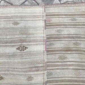 May include: A vintage rug with a striped pattern in shades of gray, beige, and brown. The rug features geometric diamond and floral motifs. The design is symmetrical, with a central vertical seam. The rug's texture appears soft and woven.