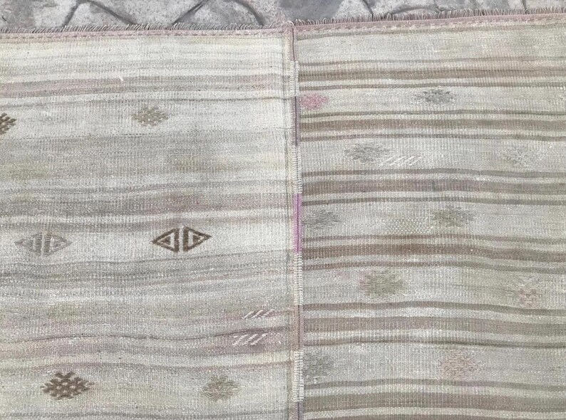 May include: A vintage rug with a striped pattern in shades of gray, beige, and brown. The rug features geometric diamond and floral motifs. The design is symmetrical, with a central vertical seam. The rug's texture appears soft and woven.
