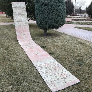 Peut inclure: Un long tapis de couleur crème avec un motif floral rose et blanc. Le tapis est posé sur une pelouse.