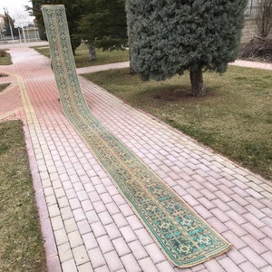 Pode incluir: Um tapete longo, verde e bege com padrões está colocado em um caminho de tijolos. O tapete está dobrado ao meio e está colocado em um caminho de tijolos.
