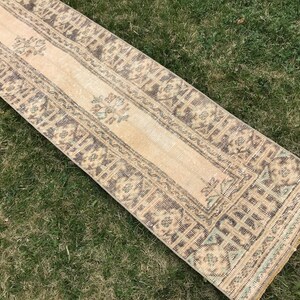 Pu&ograve; includere: Un tappeto da corridoio beige con un motivo geometrico marrone e blu. Il tappeto ha un aspetto vissuto ed &egrave; realizzato in un materiale morbido e tessuto.
