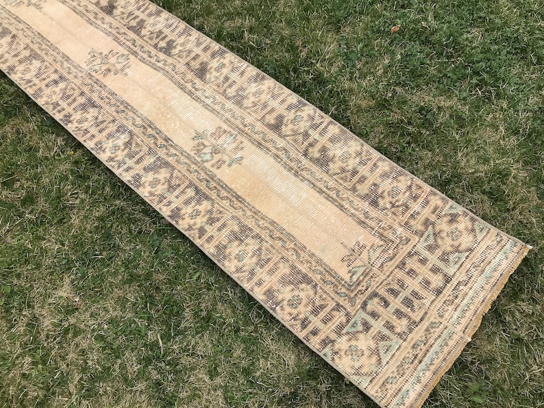 Pu&ograve; includere: Un tappeto da corridoio beige con un motivo geometrico marrone e blu. Il tappeto ha un aspetto vissuto ed &egrave; realizzato in un materiale morbido e tessuto.