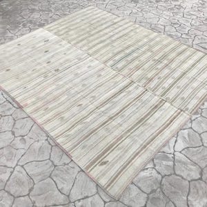 May include: A large, rectangular rug with a striped pattern in shades of cream, beige, and muted green. The rug is divided into several sections and has a subtle, faded appearance. The design features vertical stripes with occasional small, circular motifs.