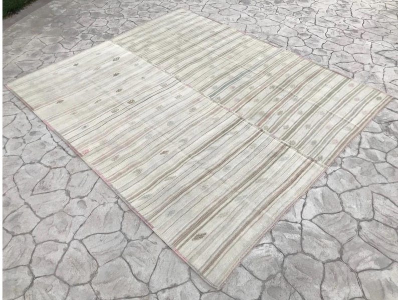 May include: A large, rectangular rug with a striped pattern in shades of cream, beige, and muted green. The rug is divided into several sections and has a subtle, faded appearance. The design features vertical stripes with occasional small, circular motifs.