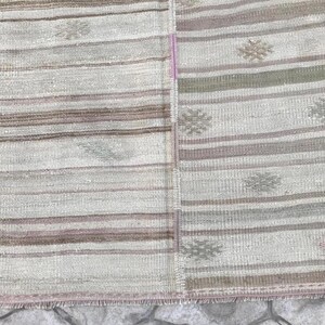 May include: A rectangular, woven rug with a patchwork design. The rug features horizontal stripes in shades of beige, brown, and gray. Floral-like patterns are scattered across the surface. The edges have a fringed border.