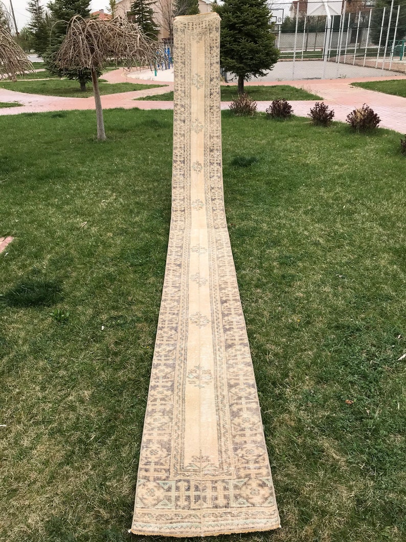 Pu&ograve; includere: Un tappeto da corridoio lungo e beige con un motivo geometrico in tonalit&agrave; di marrone e blu. Il tappeto &egrave; piegato a met&agrave; e steso su un prato.
