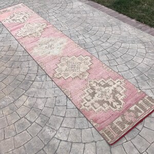 May include: A pink and cream runner rug with a traditional geometric pattern. The rug has a distressed look and is made of a soft, woven material.