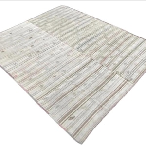 May include: A rectangular, light-colored rug with a striped pattern. The rug features vertical stripes in shades of white, gray, and brown. Small, circular, decorative elements are interspersed throughout the design. The rug is likely made of woven fabric.