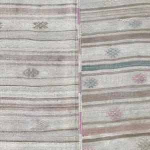 May include: A close-up of a section of a rug with a striped pattern in shades of gray, brown, and pink. The rug has small, repeating floral-like designs. The texture of the rug is visible, suggesting a woven construction.