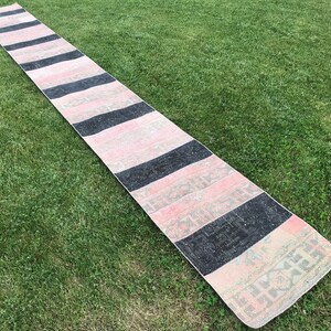 May include: A long, narrow rug with alternating black and pink stripes. The rug has a faded, vintage look and is made of a soft, woven material.