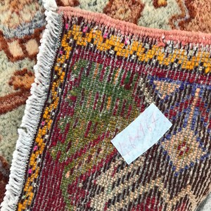 May include: A close-up of a colorful rug with a white fringe. The rug has a geometric pattern with red, blue, green, and yellow colors. A white note with the text "4x4ft" is attached to the rug.