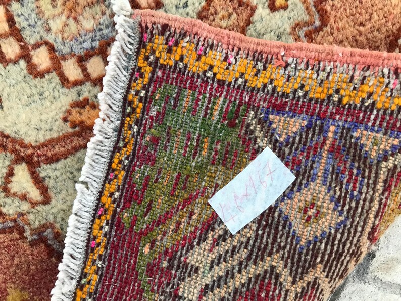 May include: A close-up of a colorful rug with a white fringe. The rug has a geometric pattern with red, blue, green, and yellow colors. A white note with the text "4x4ft" is attached to the rug.