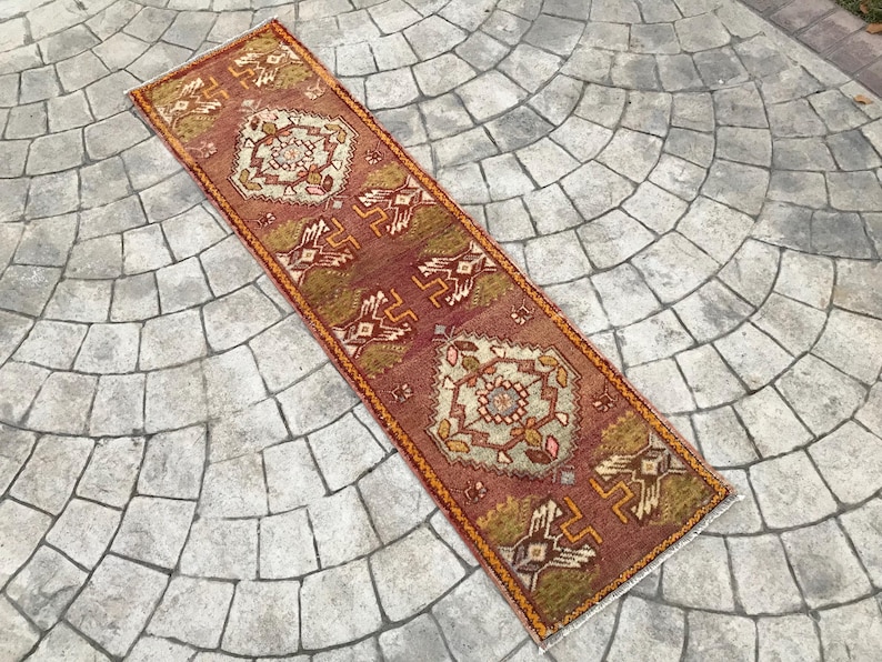 May include: A long, narrow rug with a traditional Turkish design. The rug is red, orange, and cream with a geometric pattern.