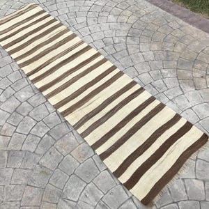 May include: A long, narrow, striped rug with alternating brown and white stripes. The rug is made of a soft, natural fiber and has a fringed edge.