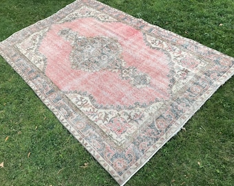 May include: A vintage pink and cream rug with a floral pattern and a gray border. The rug is laid out on a green grassy lawn.