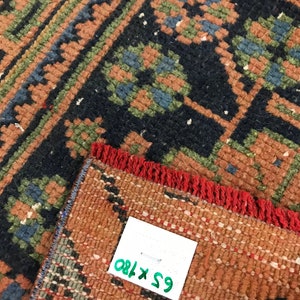 Może przedstawiać: Zbliżenie na czerwony, zielony i niebieski dywan z frędzlami. Do dywanu przymocowana jest biała metka z tekstem "65 x 180".