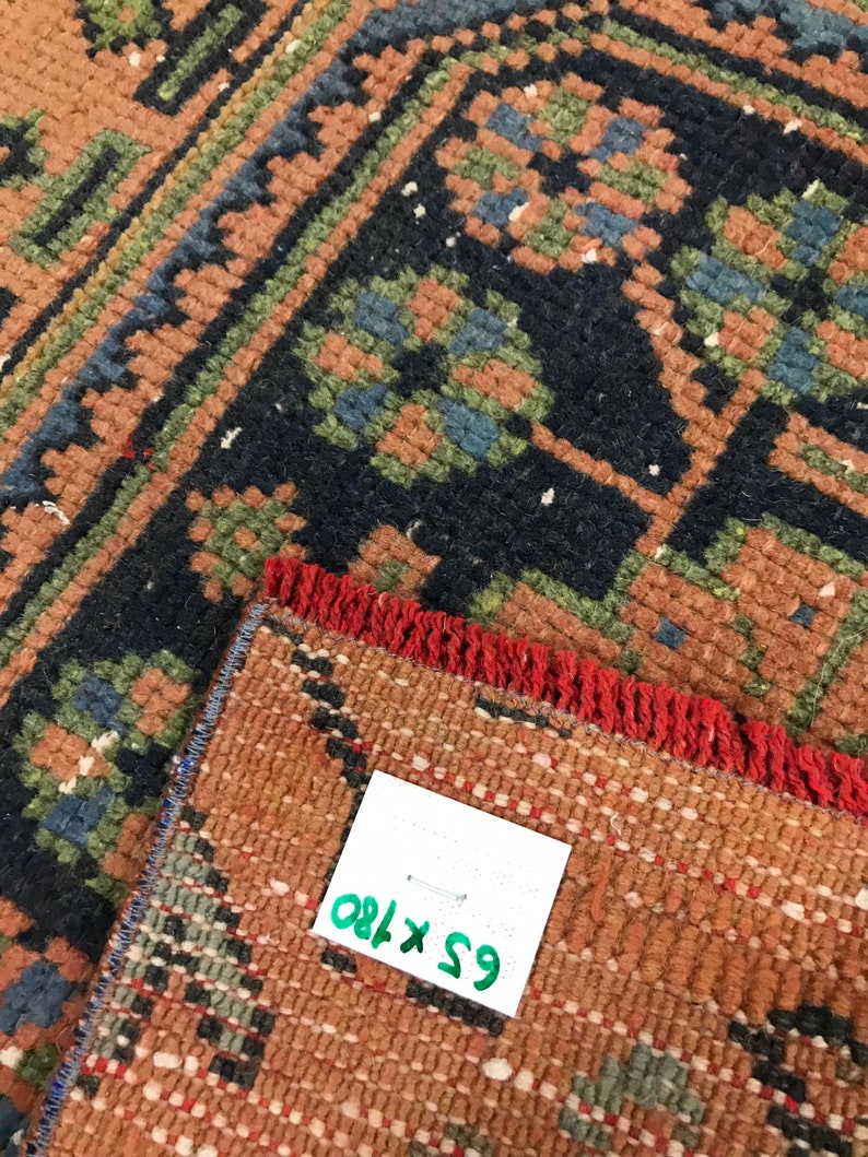Może przedstawiać: Zbliżenie na czerwony, zielony i niebieski dywan z frędzlami. Do dywanu przymocowana jest biała metka z tekstem "65 x 180".