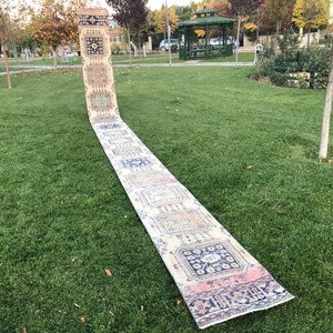 May include: A long, cream-colored rug with a colorful geometric pattern. The rug is laid out on a green lawn.