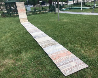 May include: A long, rectangular rug with a patchwork design in shades of beige, cream, and light blue. The rug is laid out on a grassy lawn.