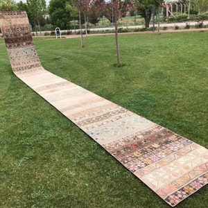 May include: A long, narrow, beige and brown patterned rug laid out on a green grassy lawn.