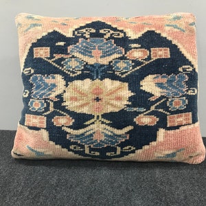 May include: Square decorative pillow with a floral pattern. The pillow features a navy blue center with a cream and pink floral design. The edges are a light pink color. The pillow is made of a woven fabric.