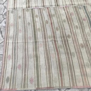 May include: A rectangular rug with vertical stripes in shades of beige, pink, green, and gray. The rug has a faded, vintage appearance with small floral-like patterns scattered throughout. The edges are finished with a pink border.
