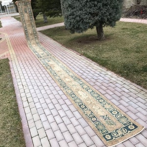 May include: A long, beige runner rug with a floral pattern in shades of green and blue. The rug is laid out on a brick walkway.