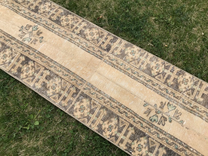 Pu&ograve; includere: Un tappeto da runner vintage con sfondo beige e motivi geometrici marroni e verdi. Il tappeto ha un aspetto vissuto ed &egrave; perfetto per aggiungere un tocco di stile boh&eacute;mien alla tua casa.