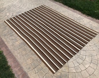 May include: A striped rug with brown and white stripes. The rug is made of a woven material and has a slightly textured surface.