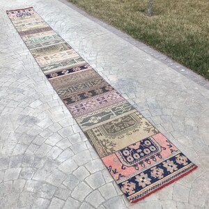 May include: A long, narrow rug with a patchwork design. The rug is made up of several different strips of fabric, each with a unique pattern. The rug is in shades of pink, brown, beige, and blue.