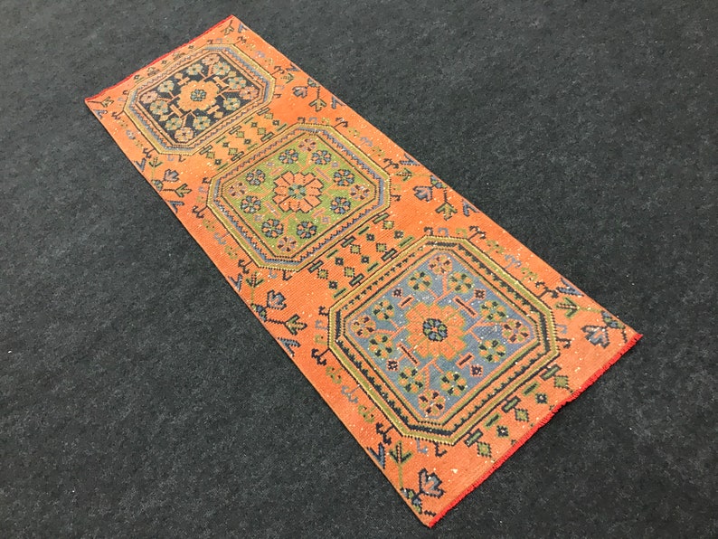 Może przedstawiać: Długi, prostokątny dywan z brzoskwiniowym tłem i trzema skomplikowanymi, kolorowymi wzorami geometrycznymi. Dywan ma frędzlowane brzegi.