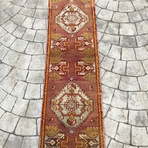 May include: A long, narrow rug with a traditional Persian design. The rug is primarily red with a cream-colored center and orange accents. The rug has a fringe on both ends.