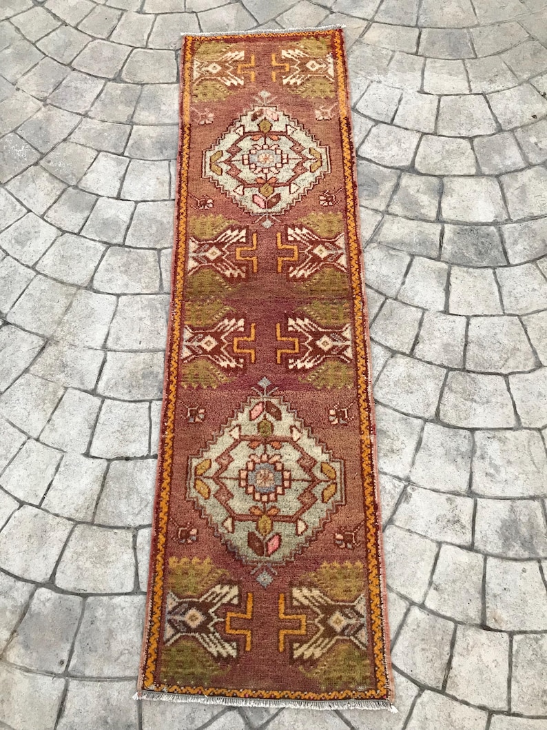 May include: A long, narrow rug with a traditional Persian design. The rug is primarily red with a cream-colored center and orange accents. The rug has a fringe on both ends.