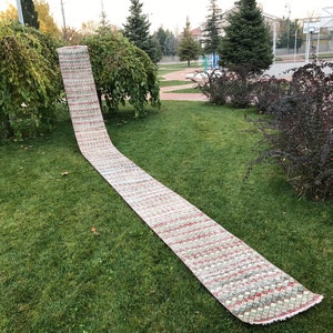 May include: A long, rectangular rug with a geometric pattern in shades of green, red, and white. The rug is laid out on a grassy lawn.