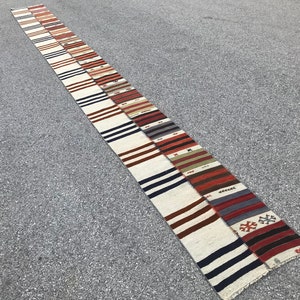 Könnte beinhalten: Ein langer, schmaler, mehrfarbiger Teppich mit weißem Hintergrund und Streifen in Rot, Braun, Blau und Grün. Der Teppich ist aus gewebtem Stoff und hat ein traditionelles Design.