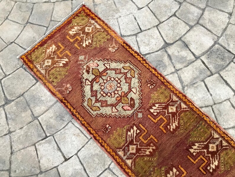 May include: A red, orange, and green patterned rug with a geometric design. The rug is rectangular and has a fringe border.