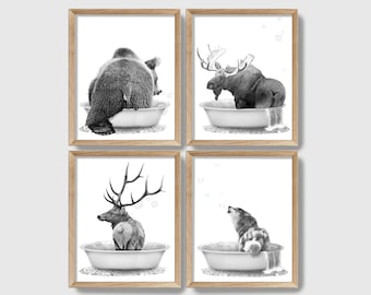 May include: Set of four black and white illustrations of animals taking a bath. A bear, a moose, a deer, and a wolf are each in a bathtub with bubbles. The prints are framed in a light wood frame.