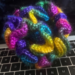 May include: A colorful crocheted ball made with multiple strands of yarn in shades of purple, blue, green, yellow, and pink.