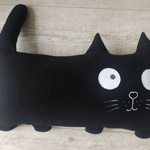 May include: Black cat-shaped pillow with white embroidered eyes, nose, and whiskers.