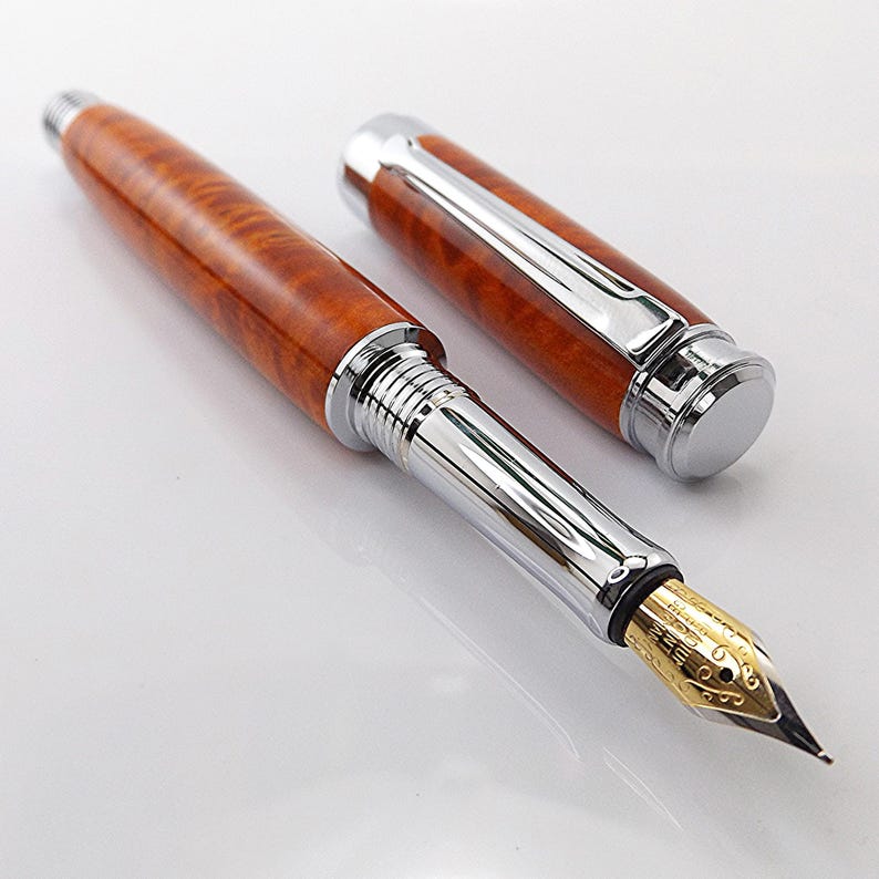 Op de afbeelding: Een luxe vulpen met een gepolijste houten schacht en een zilverkleurige metalen dop en accenten. De penpunt is goudkleurig. De pen wordt getoond zonder dop, waardoor de penpunt zichtbaar is.