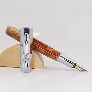 May include: A luxury fountain pen with a polished silver cap and a wooden barrel. The pen features a gold nib and is displayed on a wooden stand. The barrel has a rich, brown wood grain pattern.