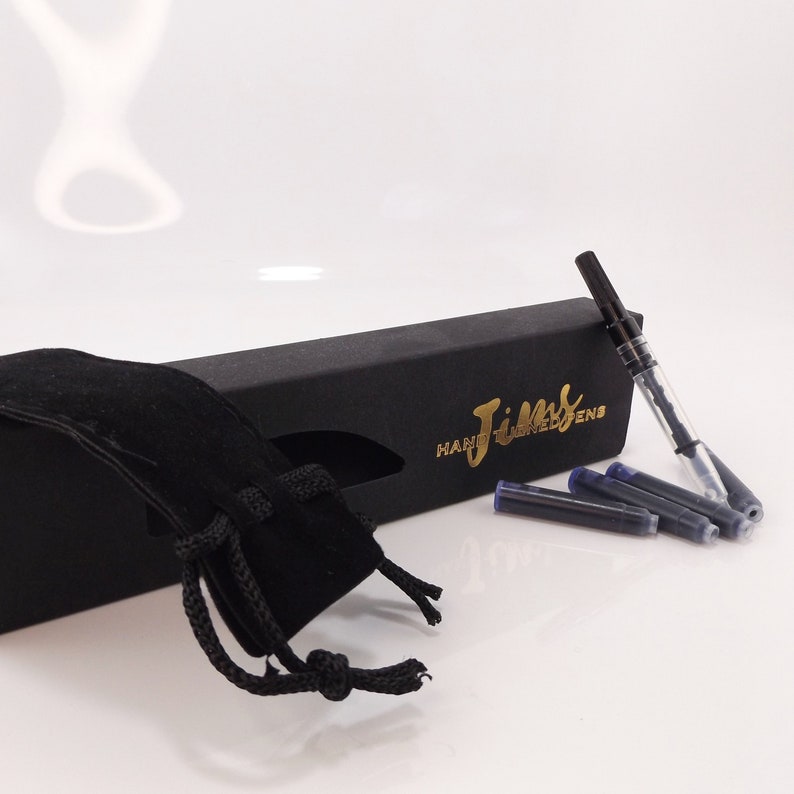 May include: A black pen set with a black box and a black velvet pouch. The box has gold lettering that reads "Jims Hand Turned Pens". Several blue ink cartridges are next to the pen.