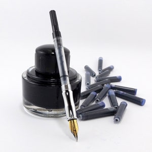 May include: A fountain pen with a gold nib, a clear barrel, and a black cap rests beside a black ink bottle and a scattering of ink cartridges. The ink is a deep black color, and the background is white.